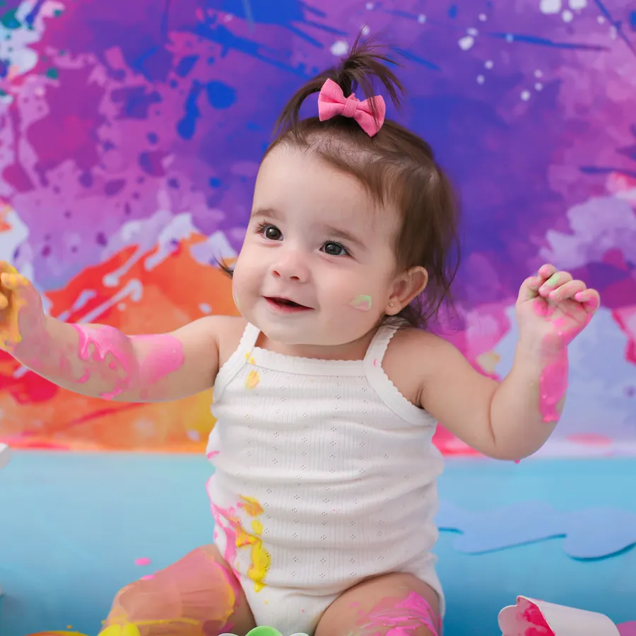 Olívia sorrindo em um cenário colorido de tintas