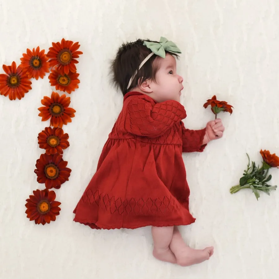 Olívia com um mês segurando uma flor laranja