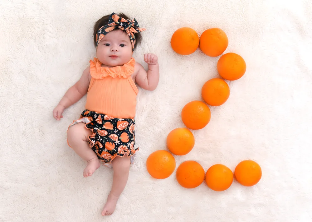 Olívia aos 2 meses ao lado de um número 2 feito de laranjas