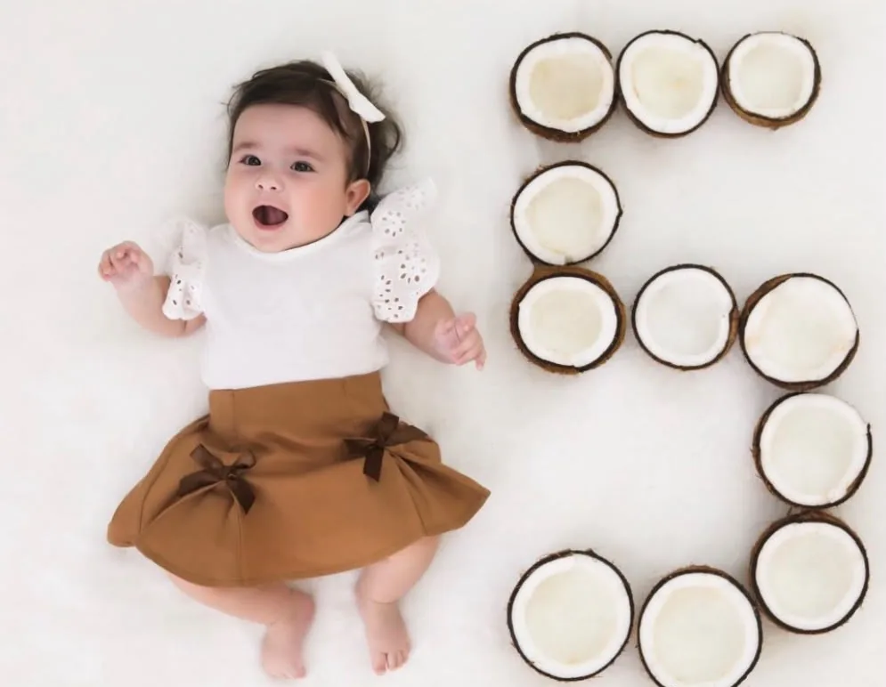 Olívia aos 5 meses ao lado de um número 5 feito de metades de coco